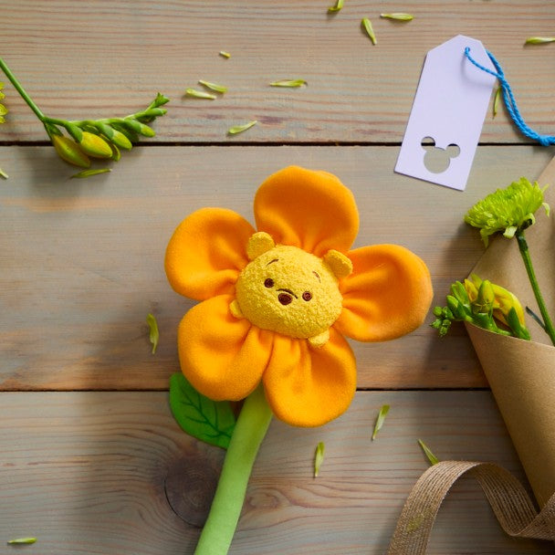 Flor de peluche Winnie the Pooh sobre una mesa de madera, junto a flores y una etiqueta de regalo