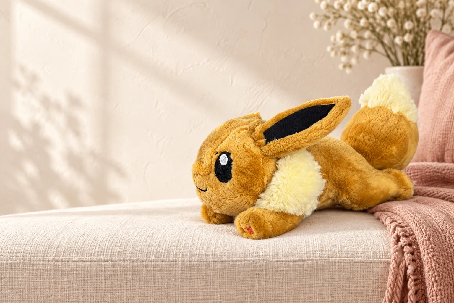 Peluche Eevee sobre un banco de lino marfil, con una manta rosada y luz natural